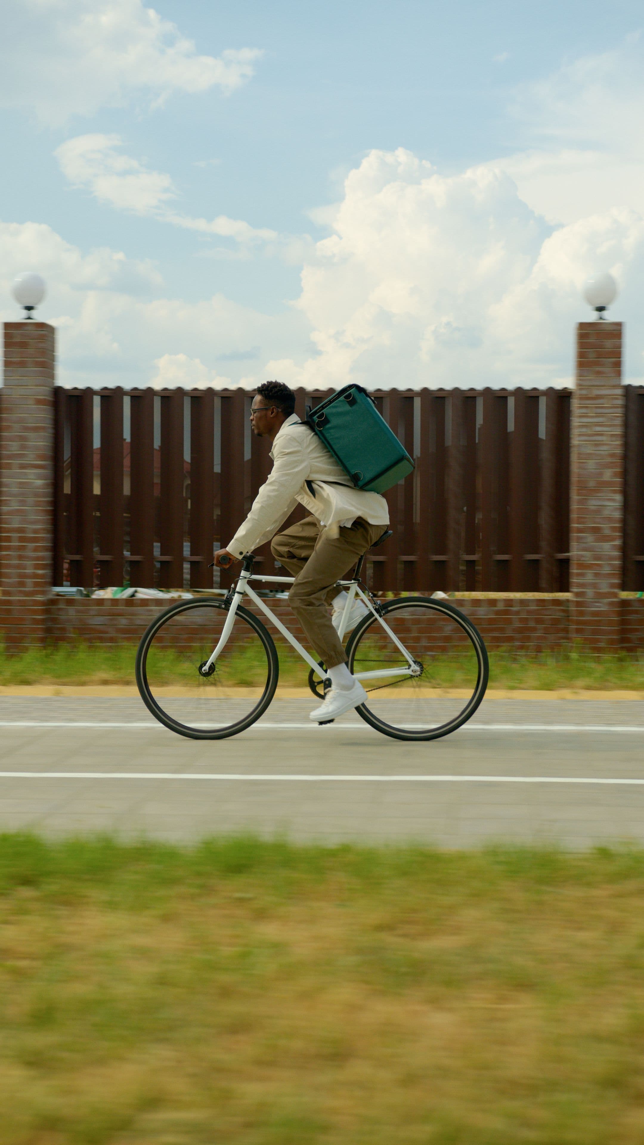 A Gereb rider riding a white bicycle along a road with a green thermal delivery box on their back.